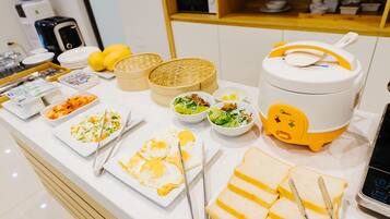 Une table de buffet proposant divers plats, notamment des œufs, des salades et du pain, ainsi qu’un cuiseur à riz.
