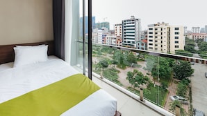 Una habitación de hotel con una cama grande, vistas de la ciudad a través de ventanales del suelo al techo y un balcón con barandilla.