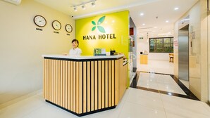 Un mostrador de recepción de hotel con diseño de madera, una pared de color amarillo brillante y relojes que marcan diferentes husos horarios.
