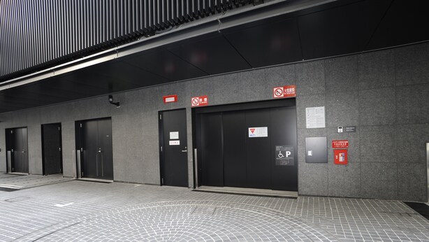 Un edificio moderno con varias puertas negras, algunas con letreros que indican prohibido fumar y acceso restringido.