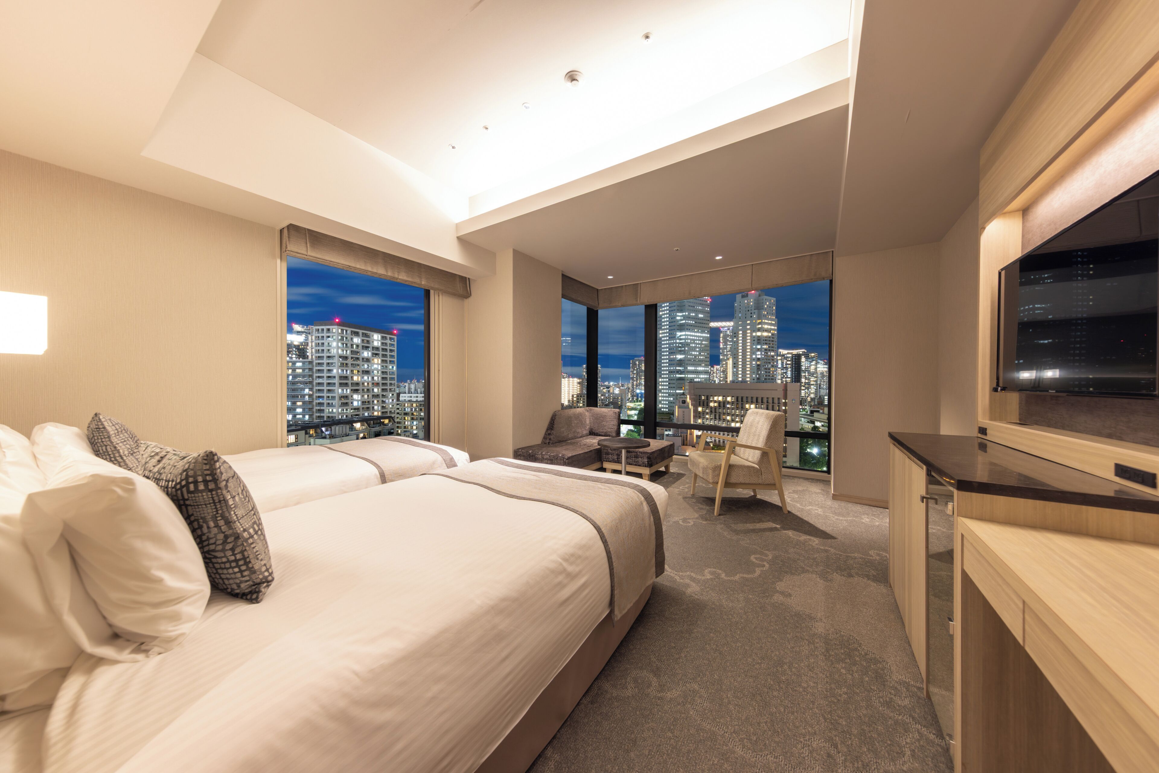 A modern hotel room with a large bed, a desk, and a view of the city skyline.