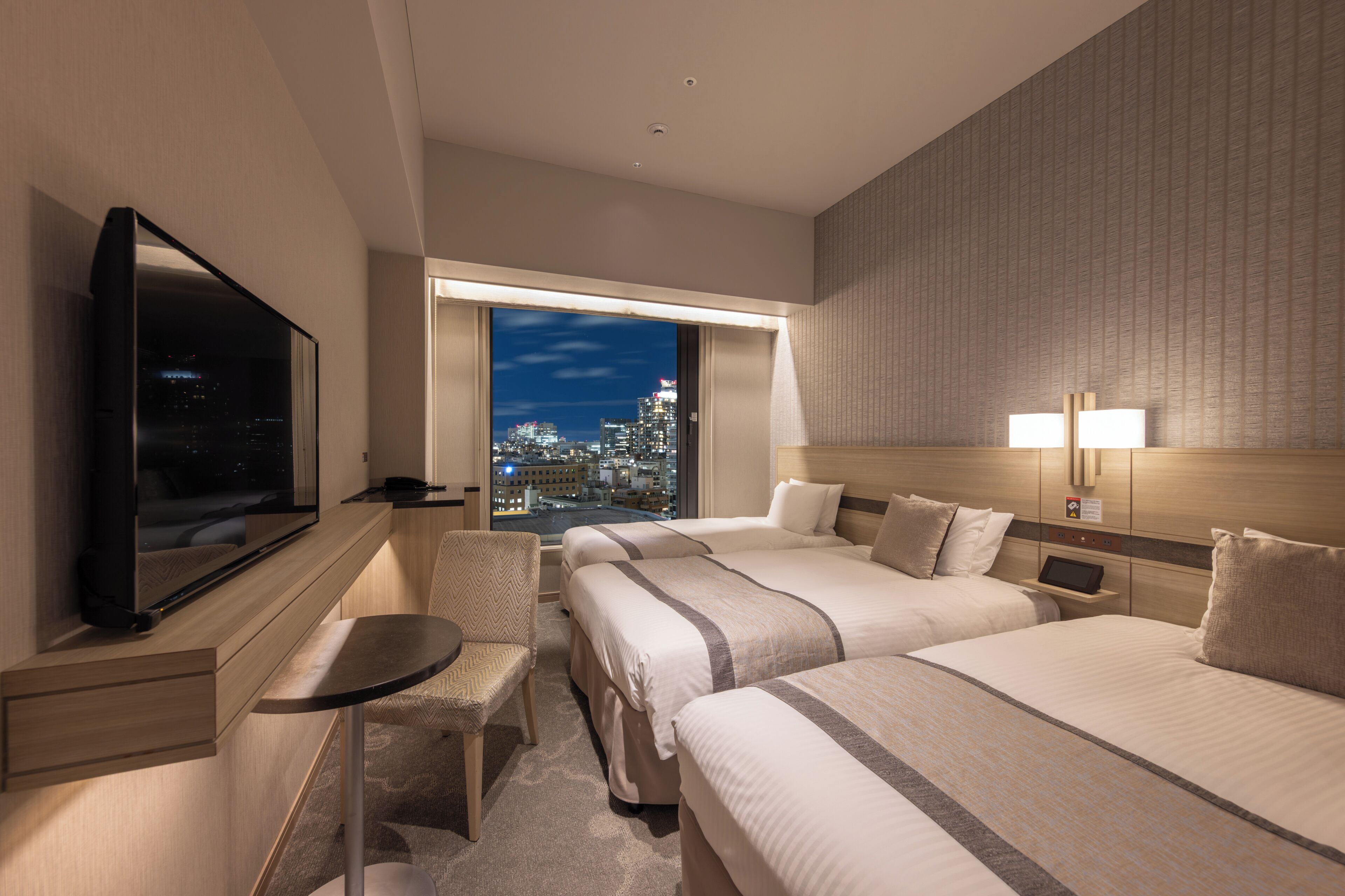 Ein Hotelzimmer mit Blick auf die Stadt, inklusive Fernseher, zwei Betten, Schreibtisch und Stuhl.