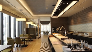 A modern hotel dining area with a buffet, seating arrangements, and a view of the cityscape. - Hotel Keihan Tsukiji Ginza Grande (Tokyo)