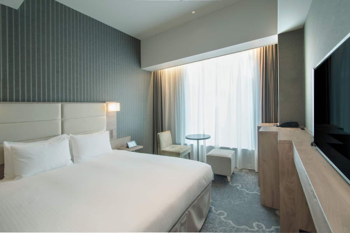 A hotel room with a large bed, a desk, a chair, a TV, and a window with curtains.