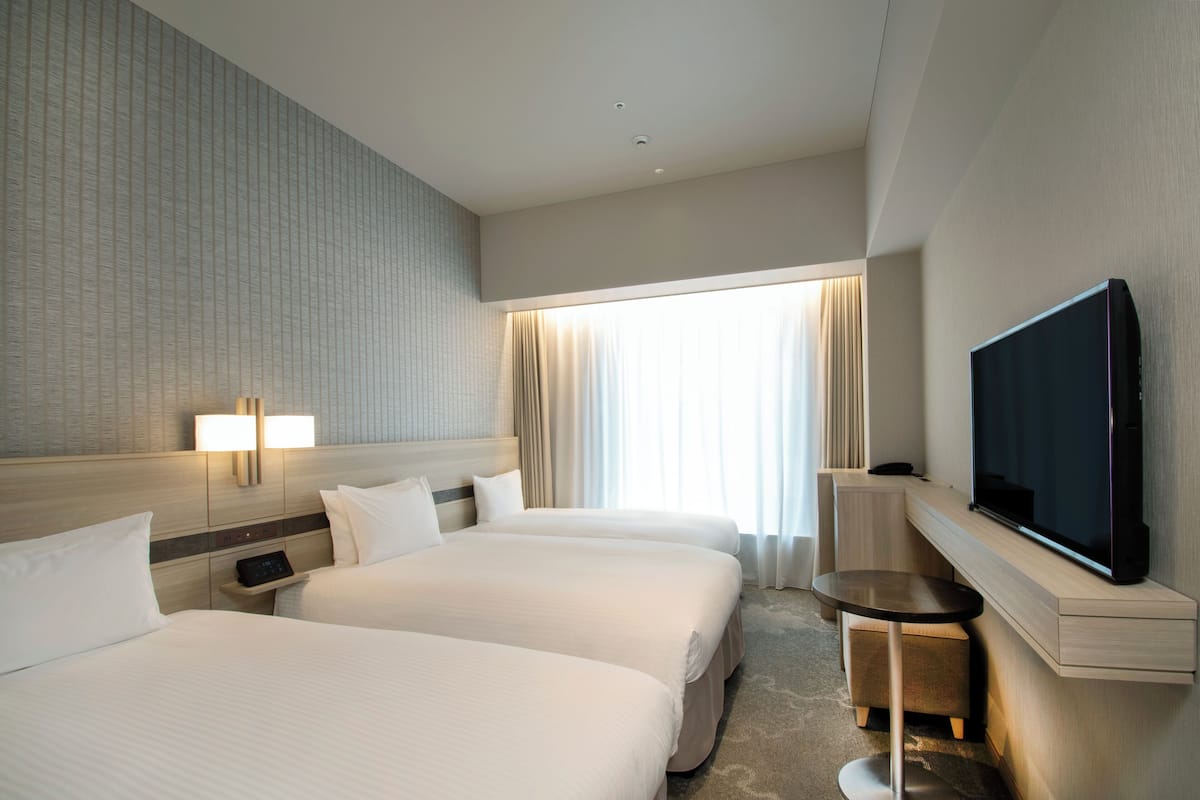 A hotel room with two beds, a TV, a bedside table, and a window with curtains.