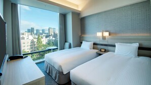 A hotel room with two beds, a desk, a chair, and a large window offering a city view. - Hotel Keihan Tsukiji Ginza Grande (Tokyo)