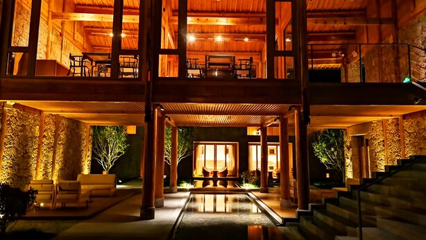 A multi-level wooden building with a central atrium, outdoor seating, and a staircase. - Tsingpu Lijiang Baisha Retreat (Lijiang)