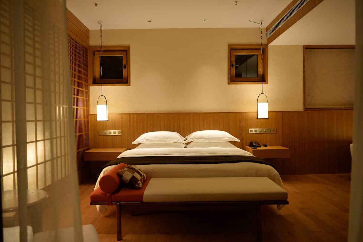 A hotel room with a bed, bedside tables, a bench, and two wall-mounted lamps.