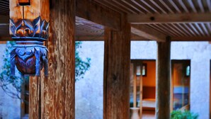 A wooden structure with carved details, a covered area with a blue floor, and a building in the background. - Tsingpu Lijiang Baisha Retreat (Lijiang)