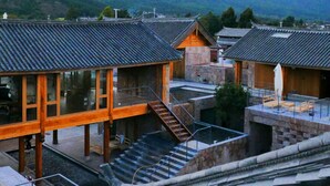 A traditional building with a wooden structure, a stone foundation, and a tiled roof. There are wooden benches and a staircase leading to an upper level. - Tsingpu Lijiang Baisha Retreat (Lijiang)