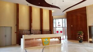 Una zona d'entrada moderna amb un taulell de recepció de fusta, un gran finestral amb detalls vermells i una planta en test.