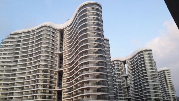 Un edifici modern i alt, amb façana corbada, múltiples balcons i un atrium central.