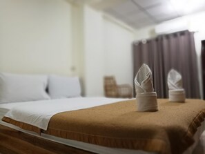 Ein ordentlich bezogenes Bett mit weißen Leinen und einem braunen Kopfteil, ein gefaltetes Handtuch auf dem Bett und ein Stuhl im Hintergrund.