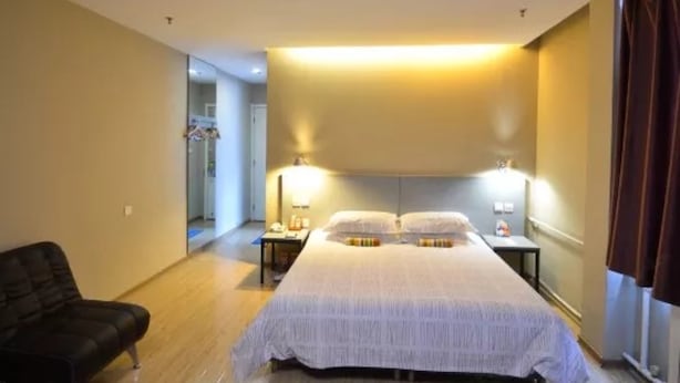Una habitación de hotel con una cama grande, lámparas de noche, una silla y un vestidor.