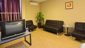 Una sala de estar con un televisor de pantalla plana sobre un mueble bajo, dos sofás de cuero, una mesita redonda pequeña, una planta en maceta y un cuadro en la pared.