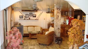 A cozy living room with a sofa, chairs, a coffee table, and a fireplace. There are framed pictures on the wall and a vase with a plant on the floor. - A&B Hotel (Hua Hin)