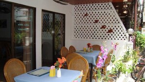 An outdoor dining area with tables covered in blue tablecloths, wicker chairs, and potted plants. - A&B Hotel (Hua Hin)