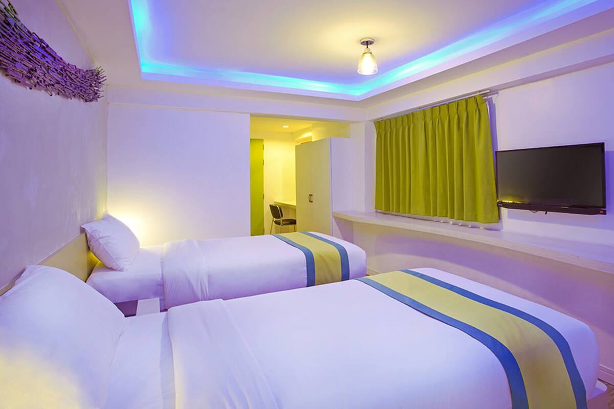Une chambre d’hôtel avec deux lits, une télévision et une salle de bain visible à travers une porte ouverte.