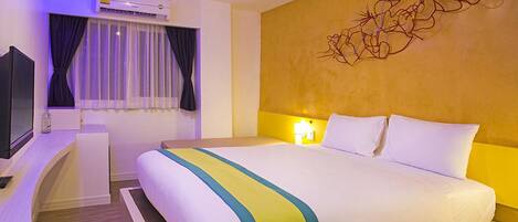 A hotel room with a bed, a desk, an air conditioning unit, a window with curtains, and a wall art piece.