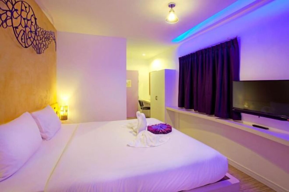 Ein Hotelzimmer mit einem großen Bett, einem Flachbildfernseher und einem im Hintergrund sichtbaren Badezimmer.
