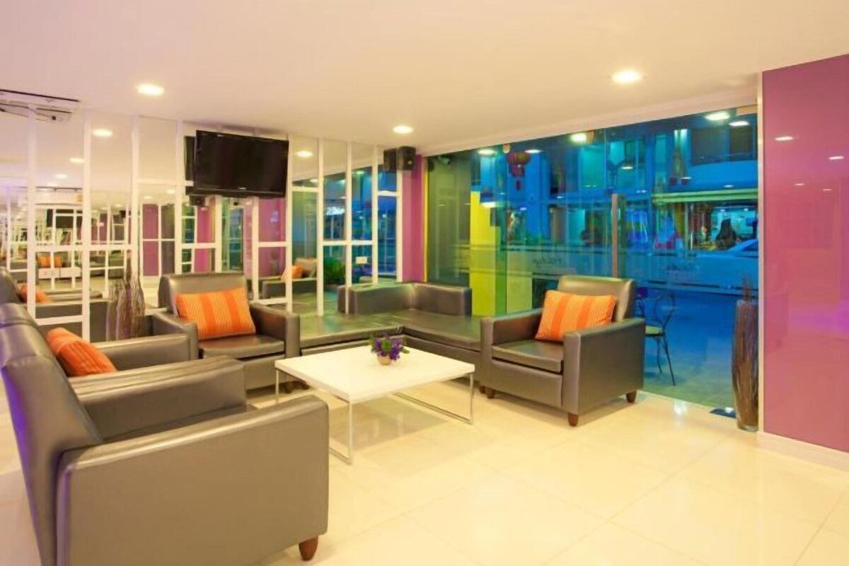 Ein moderner Lounge-Bereich mit Sofas und einem Couchtisch, große Fenster mit farbigen Glasfeldern sowie ein flachbildfernseher an der Wand.