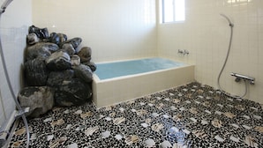 A bathroom with a bathtub, a shower, and a tiled floor with a unique pattern. - Petit House Hiromi (Minamiuonuma)