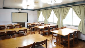 A conference room with multiple tables and chairs, a projector screen, and windows with curtains. - Petit House Hiromi (Minamiuonuma)