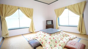 A room with tatami mat flooring, a low table, and two windows with curtains. - Petit House Hiromi (Minamiuonuma)