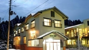 A two-story building with a sloped roof, large windows, and a visible entrance with a glass door. - Petit House Hiromi (Minamiuonuma)