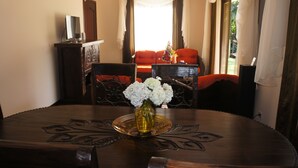 Una mesa de comedor con un florero, rodeada de sillas y un televisor sobre un mueble.