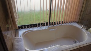 Une salle de bain avec une baignoire, une fenêtre avec des stores et une serviette sur le sol.