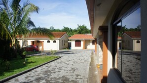 Un patio con un sendero empedrado, palmeras y un coche rojo estacionado frente a un edificio con tejado de baldosas.