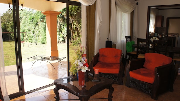 Un salón con dos sillones anaranjados, una mesa de centro de madera y un ventanal de vidrio que da a un jardín.