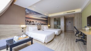 A hotel room with two beds, a desk, a chair, a table with a tray, and a painting of a sunset. - Atour Hotel Xinzhuang Shanghai (Shanghai)