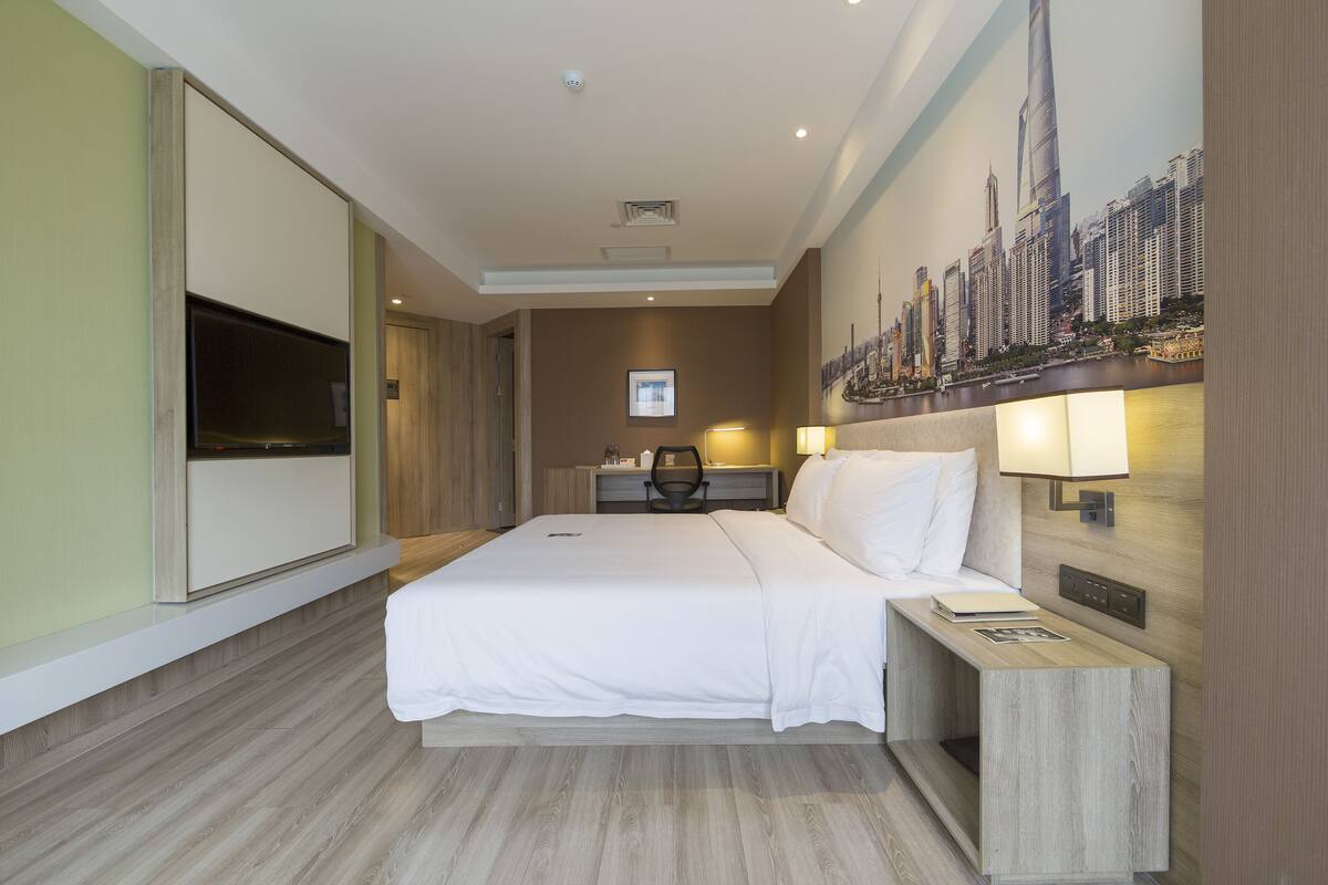 Ein Hotelzimmer mit einem großen Bett, einem Schreibtisch, einem Sessel, einem Fernseher und einer Wandmalerei mit Stadtansicht.