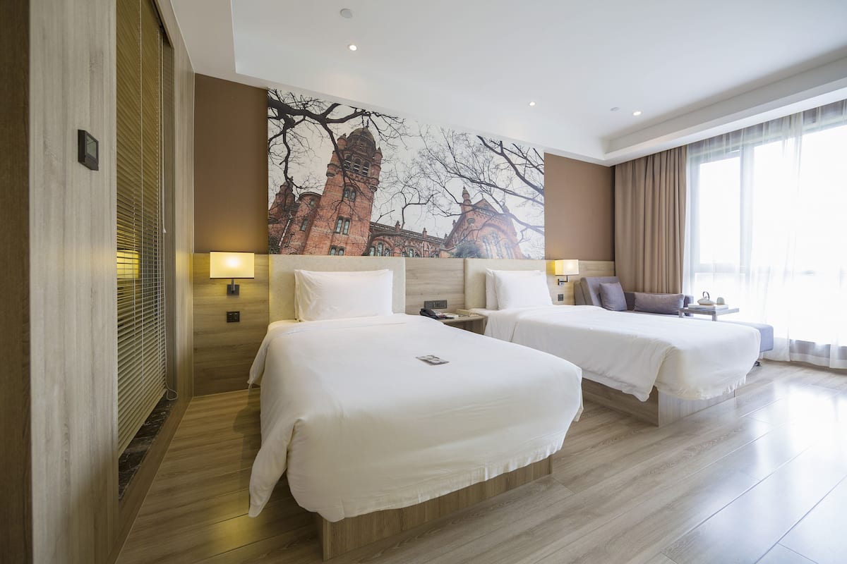 Ein Hotelzimmer mit zwei Betten, einem großen Wandbild und Blick auf ein Gebäude durch das Fenster.