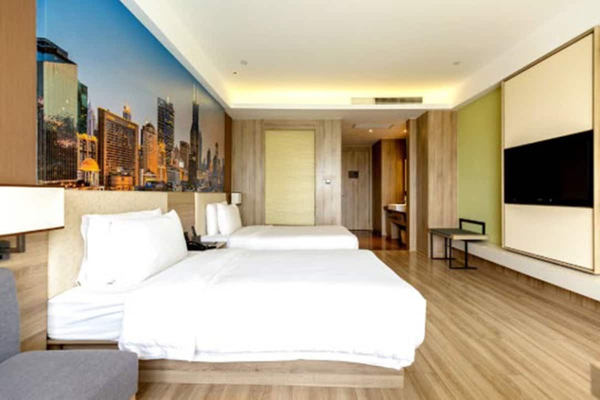 Ein Hotelzimmer mit zwei Betten, einem Stadtbild-Wandgemälde, einem Flachbildfernseher und Holzboden.