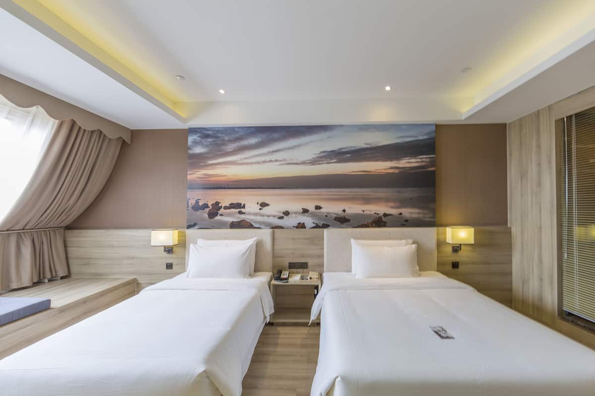 Ein Hotelzimmer mit zwei Betten, einem großen Sonnenuntergangsgemälde und Blick auf den Strand.