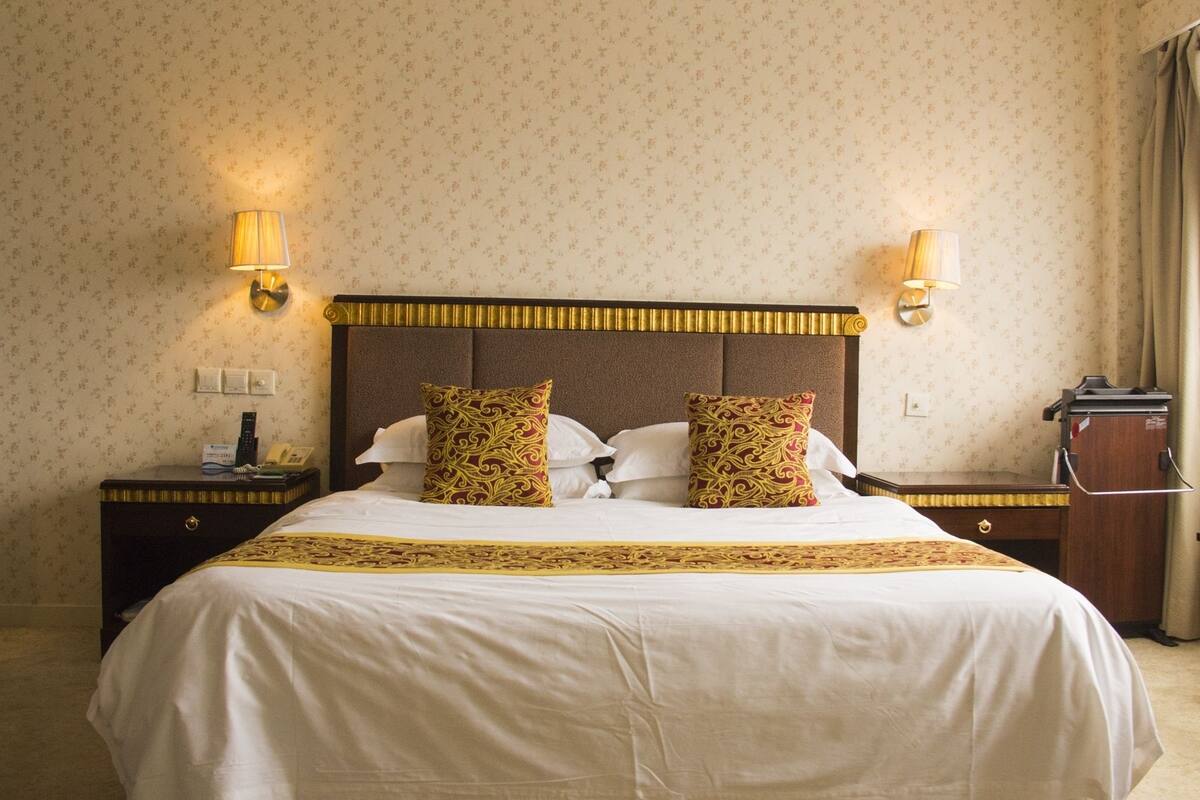 Een hotelkamer met een groot bed, twee bedlampen, een nachtkastje en een bureau met een telefoon.