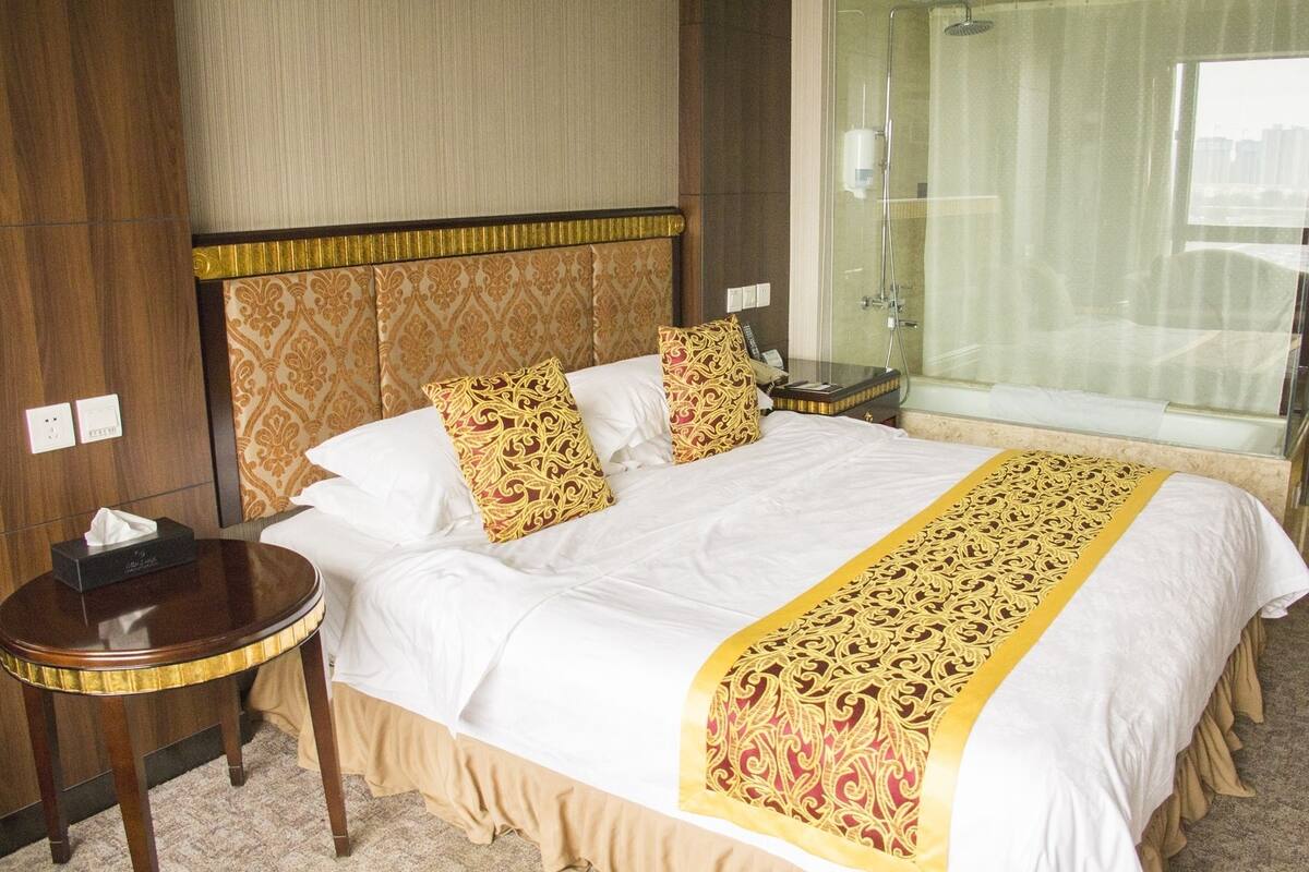 Een hotelkamer met een groot bed, twee kussens, een nachtkastje en een douchecabine met glazen wanden.