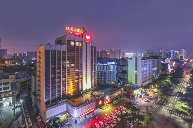 A multi-story hotel with a prominent red sign at the top, surrounded by other buildings and a busy street with parked cars.