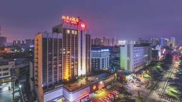 A multi-story hotel with a prominent red sign at the top, surrounded by other buildings and a busy street with parked cars.
