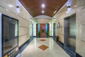 Vestíbulo de hotel con piso de mármol, ascensores y un mostrador de recepción.