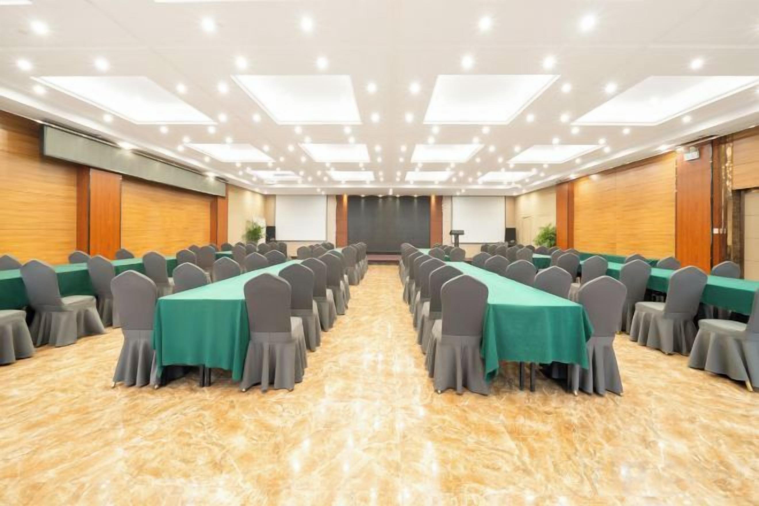 Un salón de conferencias con largas mesas, sillas y una pantalla para proyector.