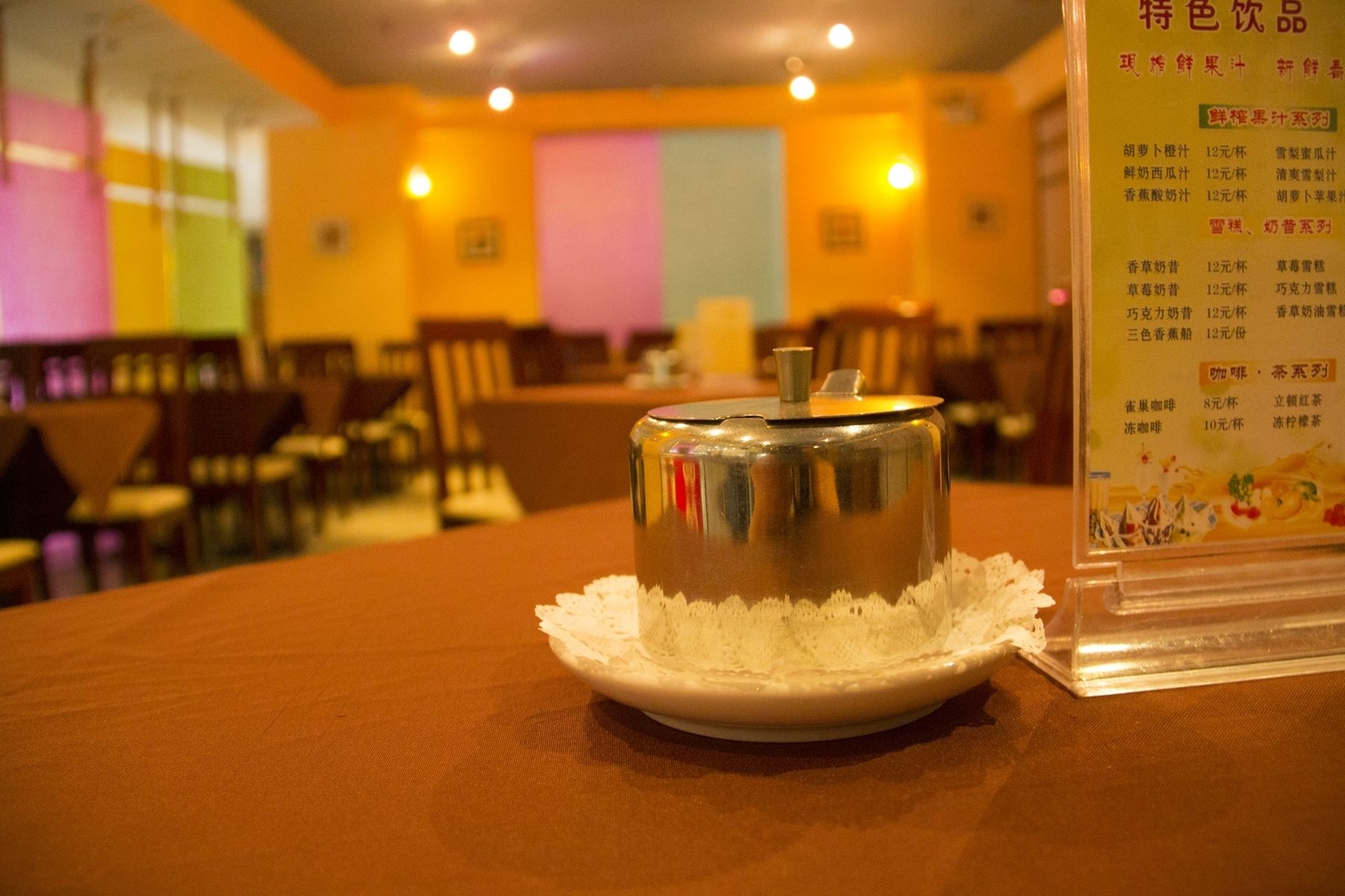 Una lata sobre un plato blanco con un mantel de encaje, un menú con opciones de comida, y un interior de restaurante con mesas y sillas.