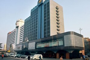 Un hotel grande con varios pisos, una destacada torre con reloj y una serie de arcos en la entrada.