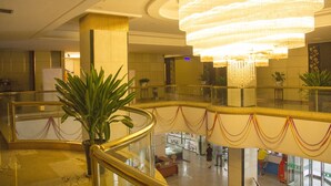A lobby with a large chandelier, a glass railing, and potted plants. - Peony Hotel (Luoyang)