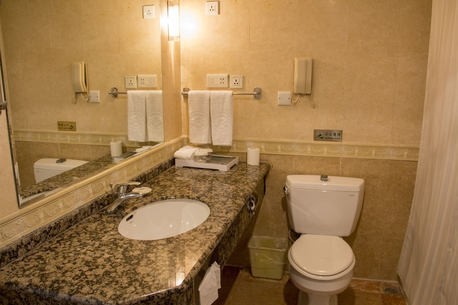 A bathroom with a granite countertop sink, a mirror, a toilet, and two wall-mounted phones.