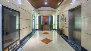 A modern hotel lobby with a marble floor, two elevators, a reception desk, and potted plants. - Peony Hotel (Luoyang)