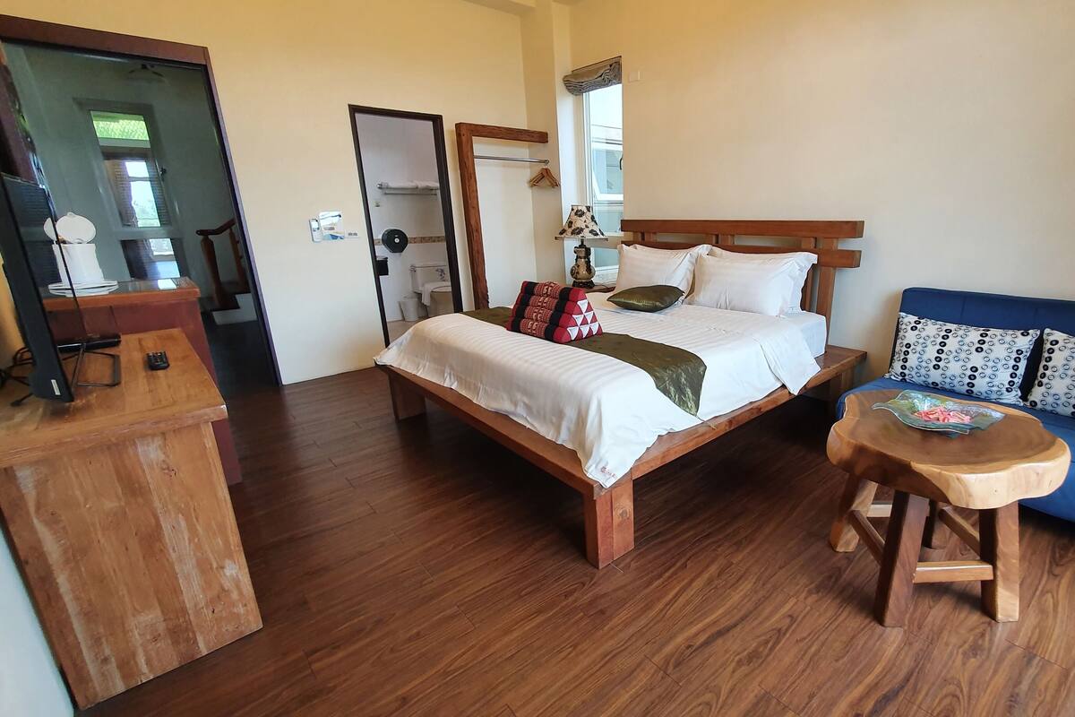 Une chambre avec un lit en bois, une table de chevet en bois, un canapé bleu et une petite table en bois.